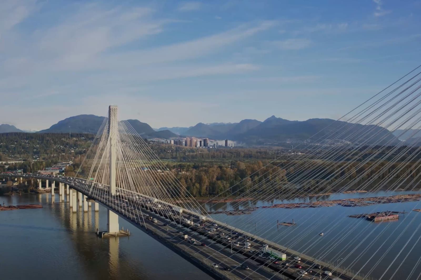 TriCity Central – Aerial photo of a cable-stayed bridge over a river with mountains and a distant city skyline in the background.