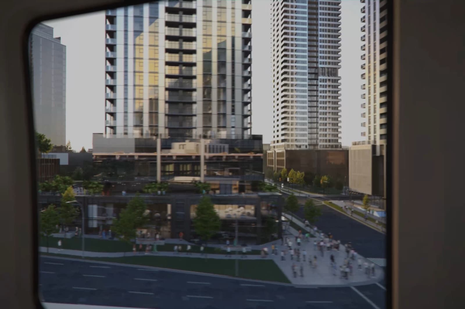 TriCity Central – View through a train window of a cluster of high-rise condo towers above a retail podium and busy plaza.