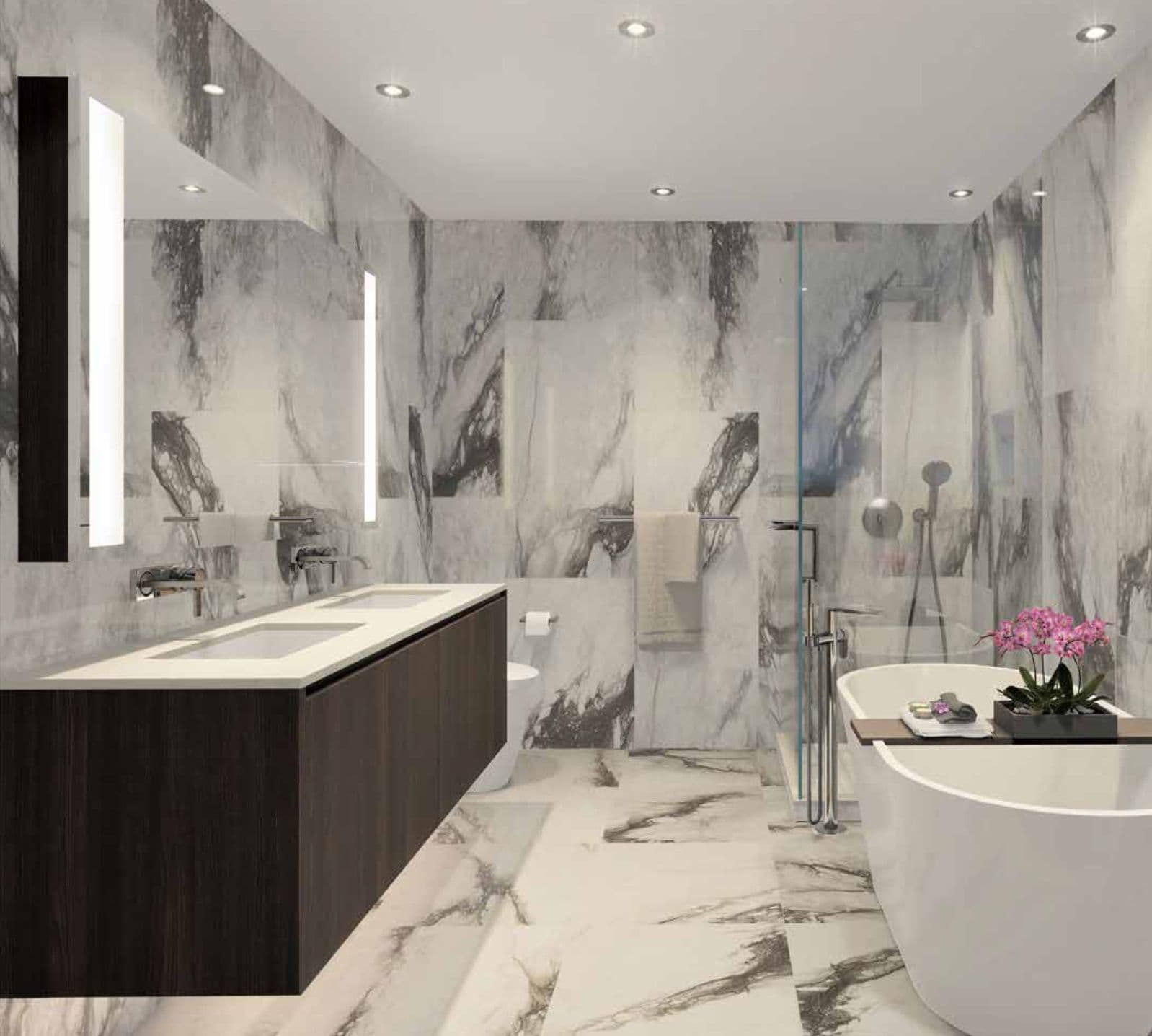 Millennium Central Lonsdale Condos – A marble-clad bathroom with a double vanity, glass-enclosed shower, wall-mounted toilet, and a freestanding soaker tub with fresh orchids.