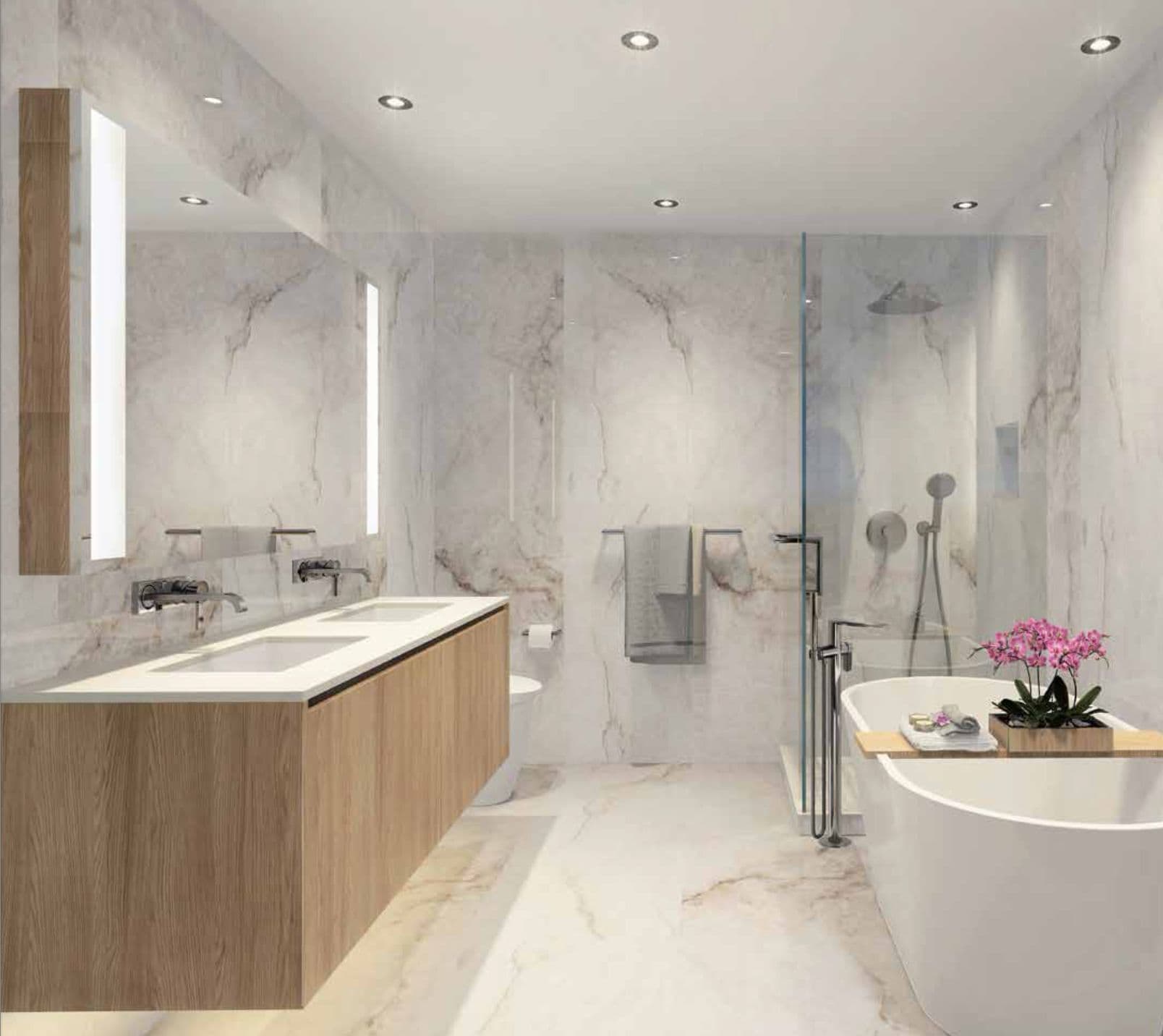 Millennium Central Lonsdale Condos – A light wood-toned bathroom with a double vanity, backlit mirrors, glass shower, and a freestanding tub decorated with orchids.