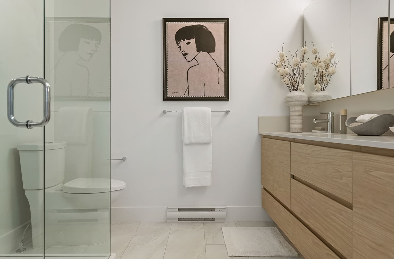 Chelsea at The Boroughs – Bathroom with a glass shower door, framed portrait art, and a towel bar, seen through a glass partition beside the toilet.