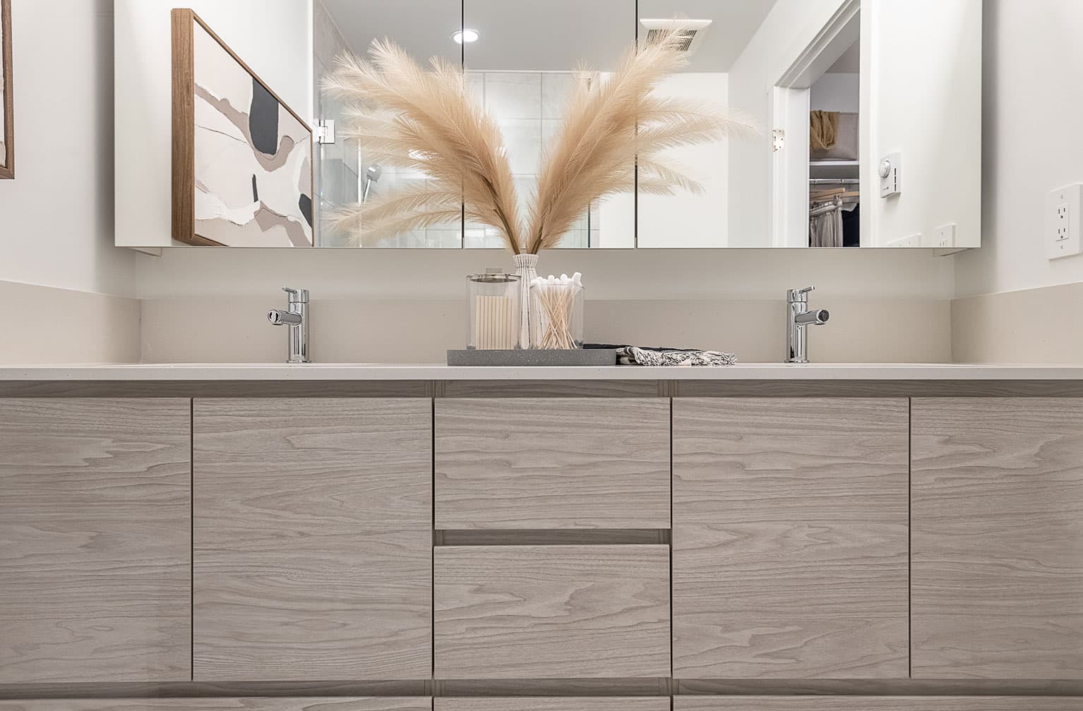 Chelsea at The Boroughs – Bathroom double-sink vanity with a wide mirror and a pampas grass arrangement between the two faucets.