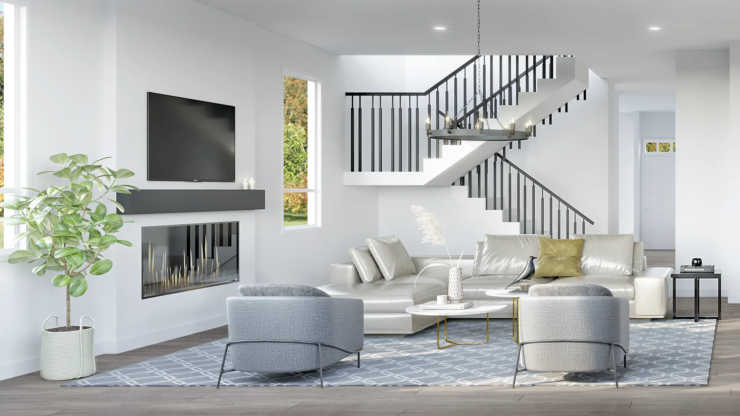Bloom at Yorkson – A bright, contemporary living room features a built-in modern fireplace with a wall-mounted TV above, paired with a light-colored sectional sofa and two grey armchairs on a patterned area rug. In the background, an open white staircase with black railings ascends under a suspended circular chandelier, with natural light pouring in from nearby windows.