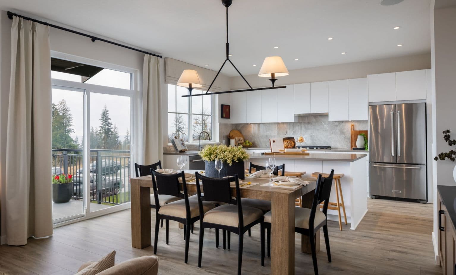 Ridgewood – Photo of a dining and kitchen space with a wood table set for a meal, black chairs, white cabinetry, a stainless refrigerator, and a sliding door to a balcony.