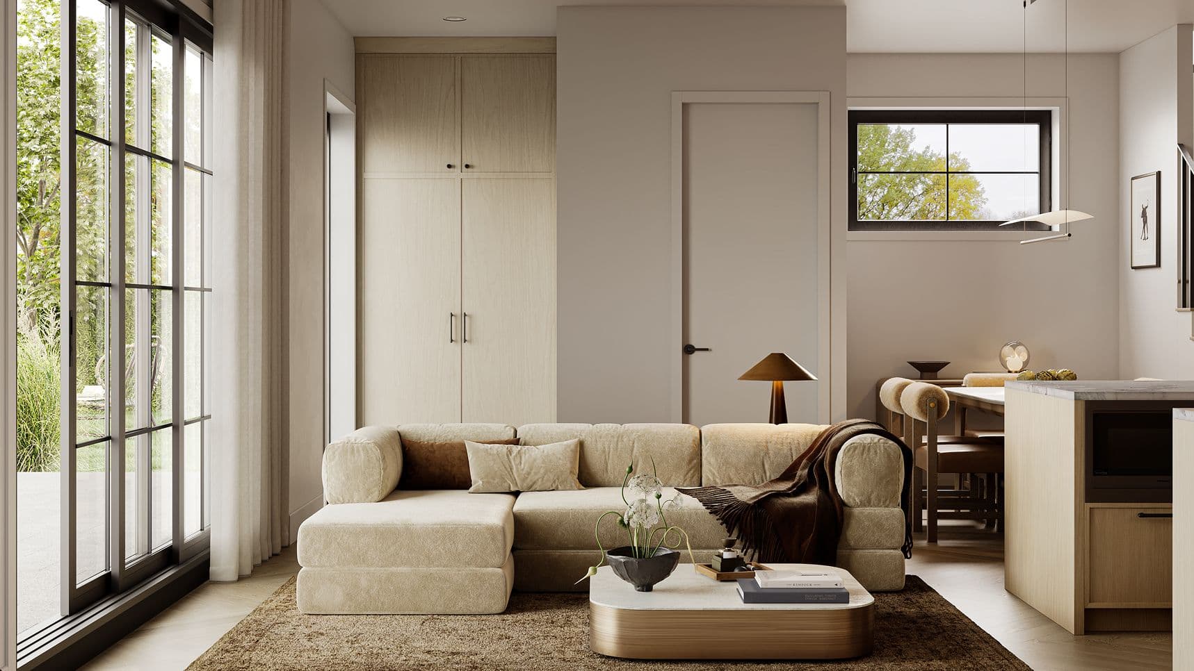 Edwyn – A warm and minimalist open-concept living area features a plush beige sectional sofa, a rounded coffee table, and tall built-in light wood cabinetry. Floor-to-ceiling glass patio doors look out onto lush garden greenery, filling the neutral-toned space with soft daytime light.