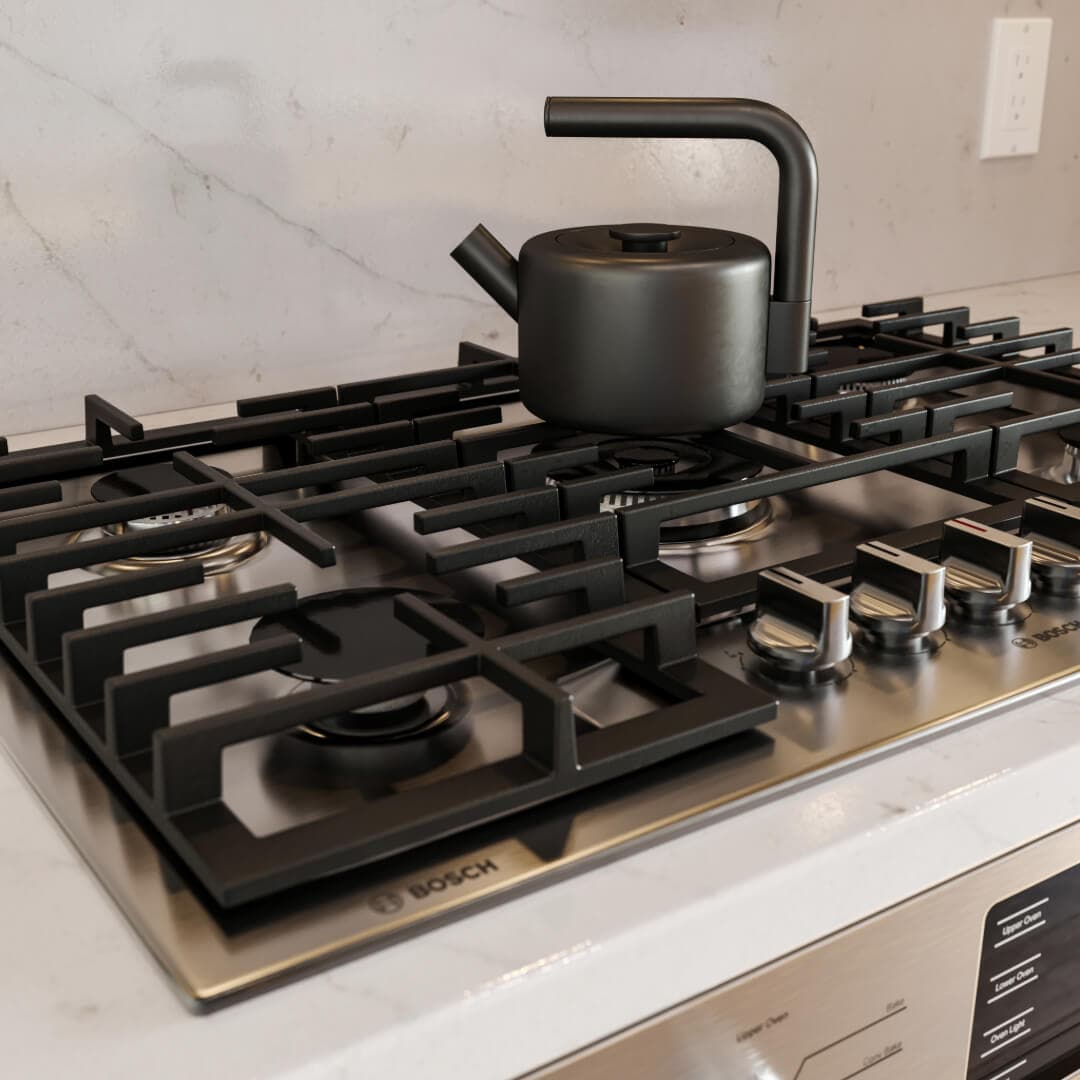 Astrid – A close-up shot features a matte black tea kettle sitting atop the cast-iron grates of a stainless steel Bosch gas cooktop. The appliance is set into a white marble countertop with subtle veining, conveying a modern and upscale kitchen aesthetic.