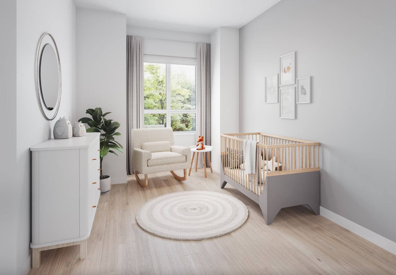 Astrid – A brightly lit modern nursery features a grey and wood crib, a white dresser with an oval mirror above it, and a comfortable rocking chair set near a large window. Soft light-colored wood flooring, neutral grey walls, a circular rug, and subtle framed artwork create a calm and serene atmosphere.