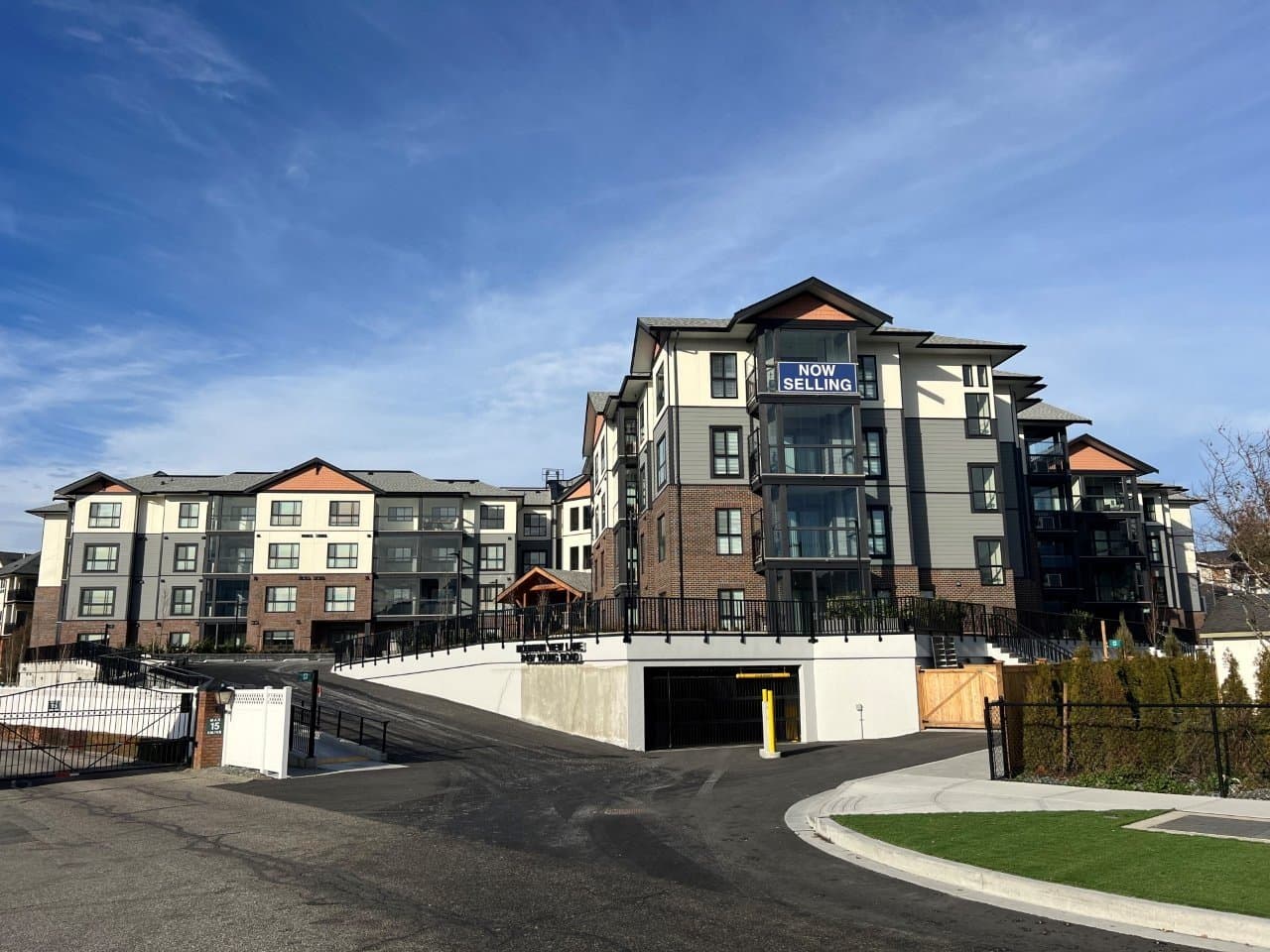 Mountainview Lane – Real daytime photo of the finished building exterior with a 'Now Selling' sign, glass balconies, and a below-grade parking garage entrance.