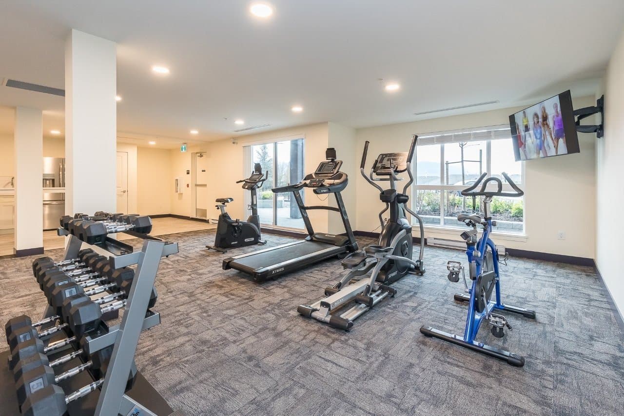 Mountainview Lane – Fitness room with a dumbbell rack, treadmill, elliptical, stationary bikes, a wall-mounted TV, and windows looking out to a mountain view.