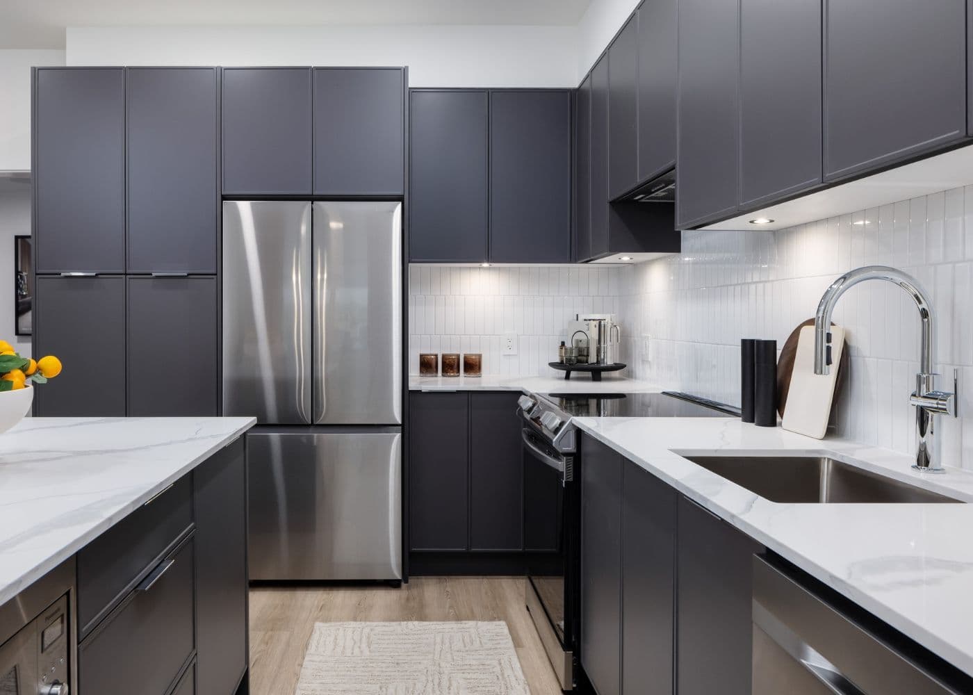 Jericho – Kitchen with dark gray cabinetry, white marble countertops, and a stainless steel refrigerator and range.