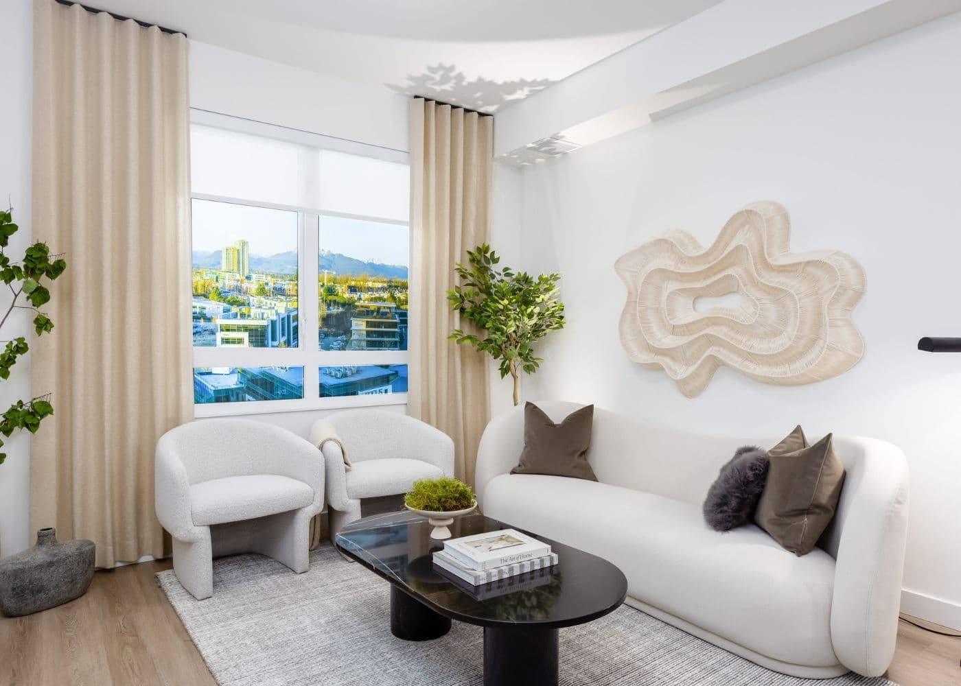 Jericho – Living room with a curved white sofa, two boucle accent chairs, and a dark oval coffee table, window showing a city and mountain view.