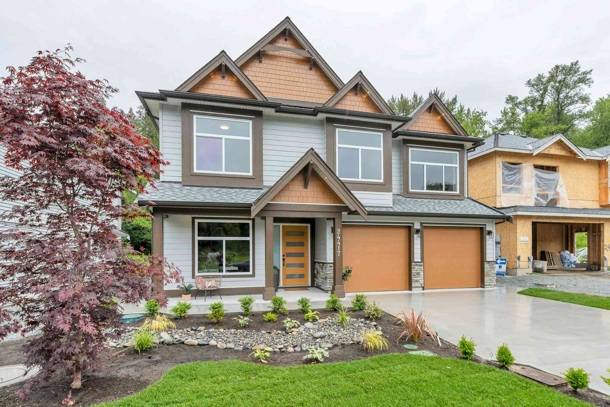 Emerald Ridge – Street-level exterior shot of a modern two-story house with wood trim accents, brown garage doors, and front landscaping.