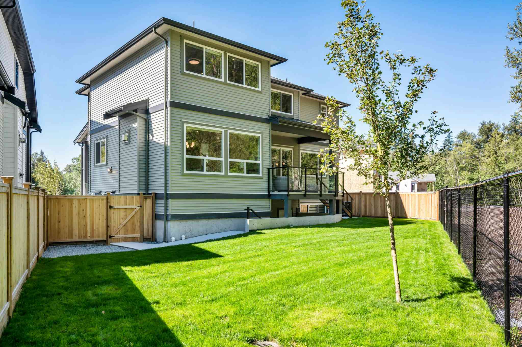Emerald Ridge – Exterior rear view of a two-story home showing a fenced grassy backyard, wooden side gate, and upper deck area.
