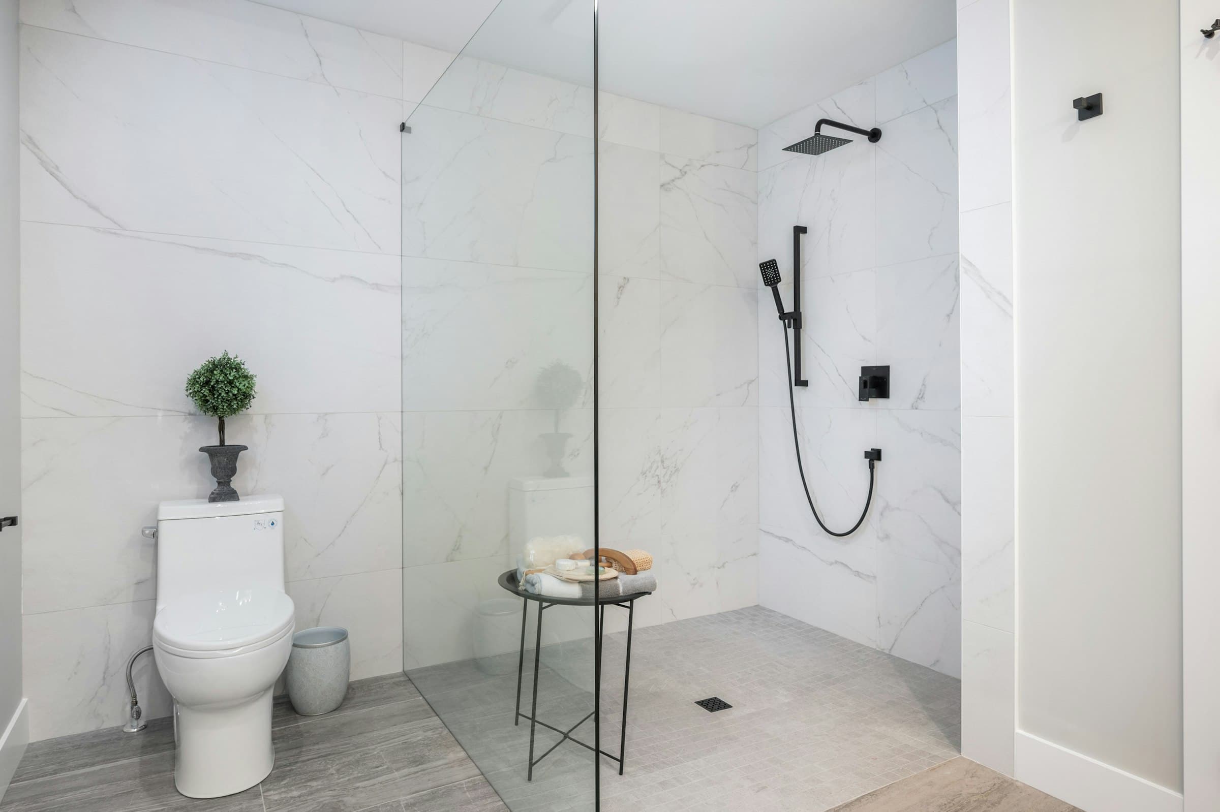 Emerald Ridge – Bathroom interior with a walk-in glass shower enclosure, matte black fixtures, marble wall tile, and modern toilet.