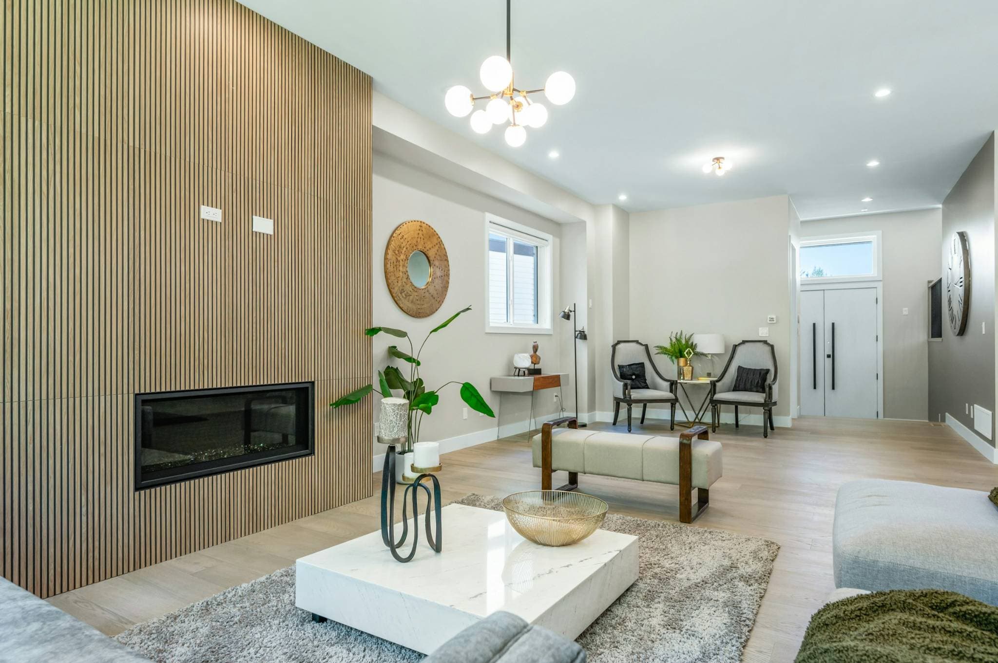 Emerald Ridge – Modern living room with a wood slat accent wall housing a built-in fireplace, marble coffee table, globe chandelier, and light wood flooring.