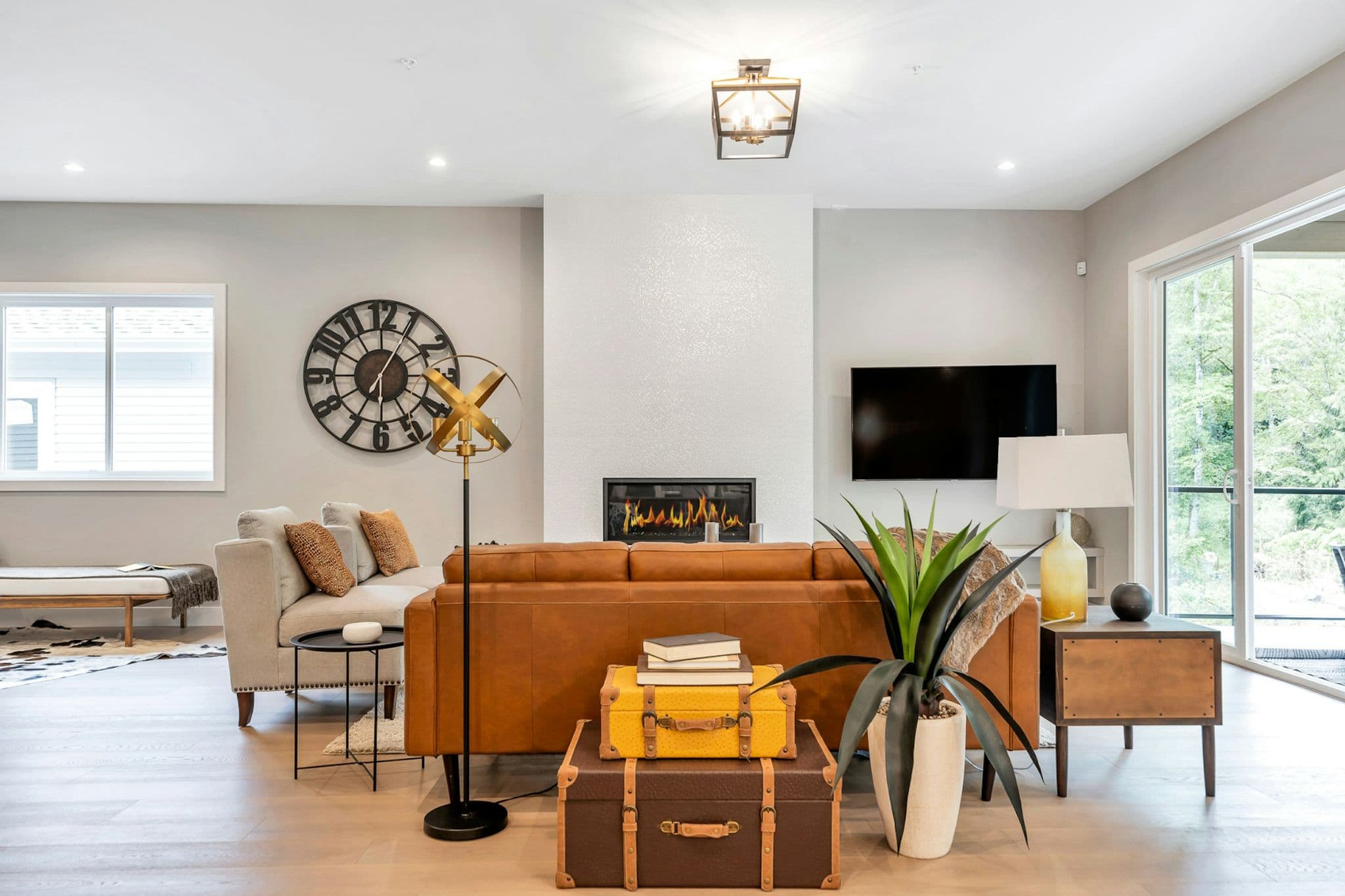 Emerald Ridge – Spacious living room featuring a leather sofa facing a linear gas fireplace, large wall clock, wall-mounted TV, and sliding glass patio doors.