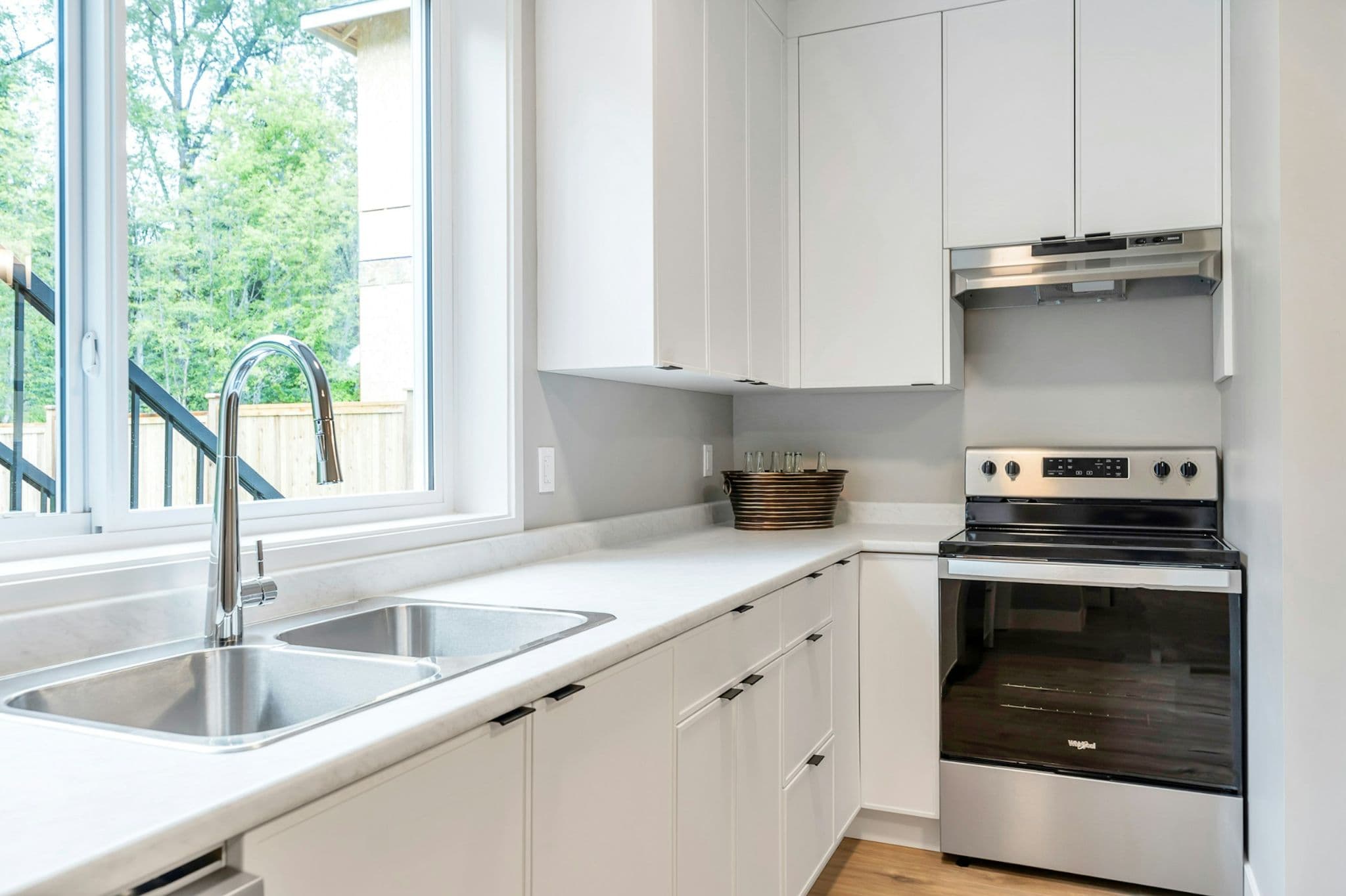 Emerald Ridge – Modern kitchen area featuring white cabinetry, stainless steel range and range hood, dual undermount sink, and large window over the counter.