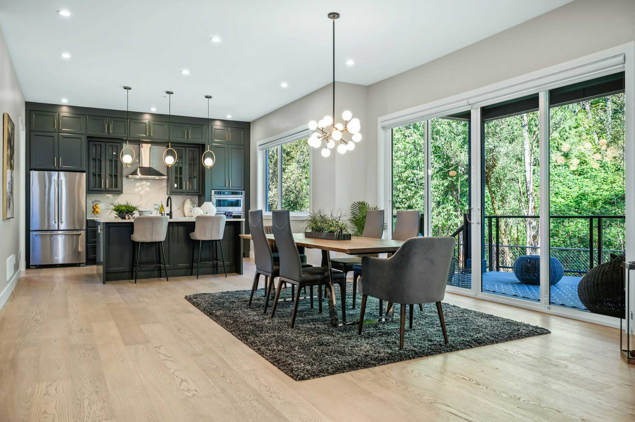 Emerald Ridge – Open-concept dining space and dark green kitchen featuring a wooden dining table, modern light fixture, kitchen island with bar seating, and sliding glass doors.