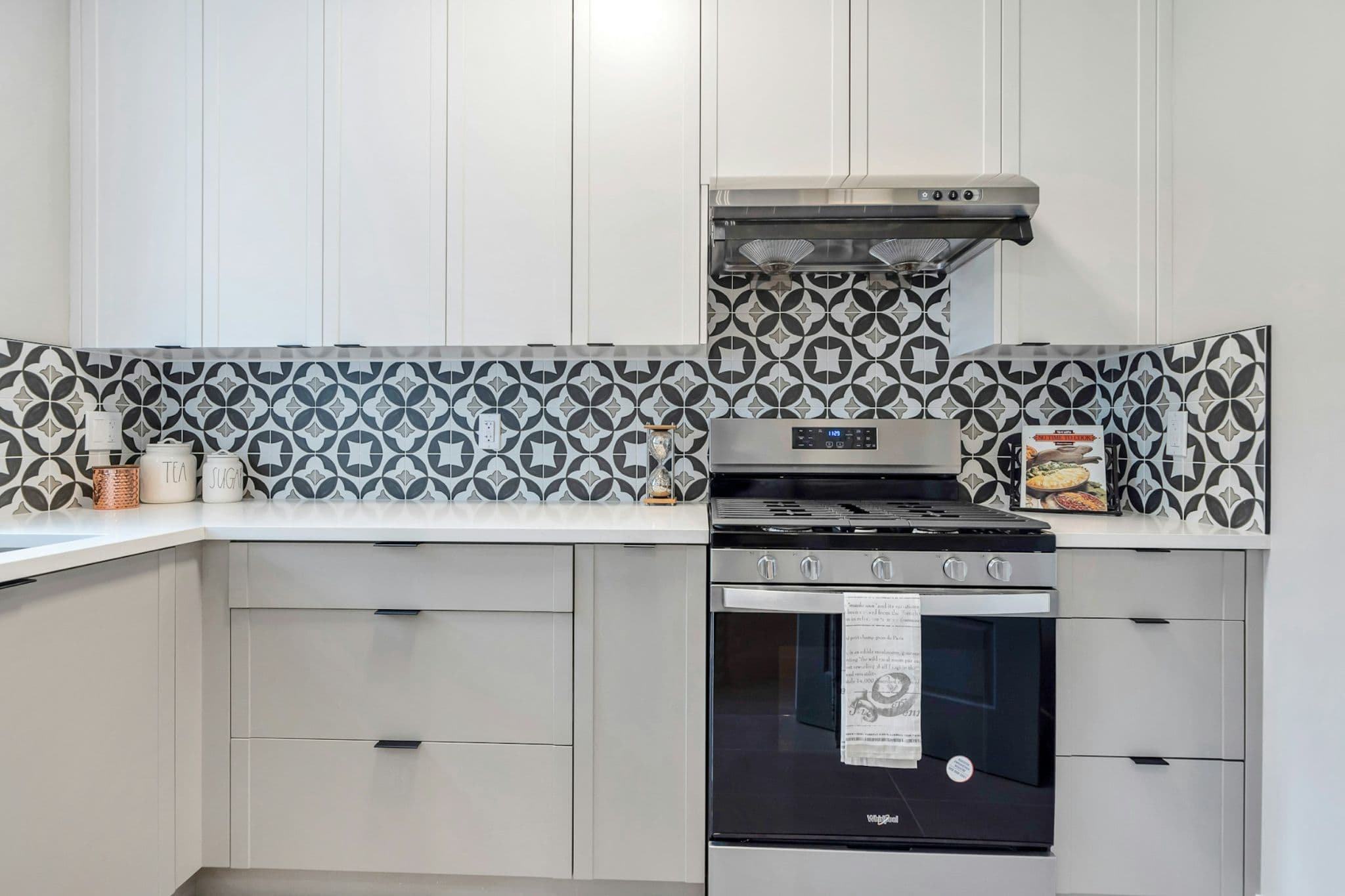 Emerald Ridge – Kitchen detail highlighting white upper cabinets, patterned tile backsplash, stainless steel gas range, and hood fan.