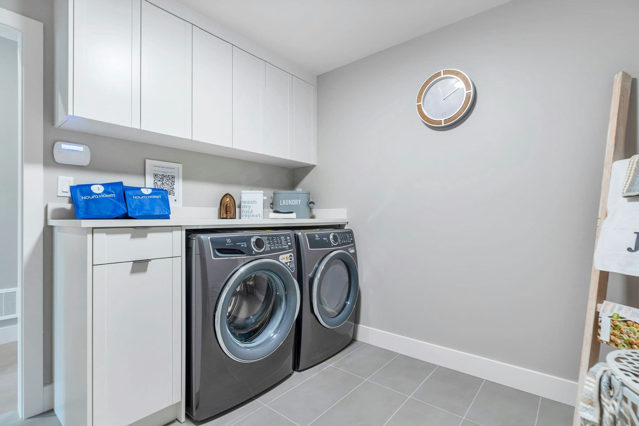 Emerald Ridge – Dedicated laundry room featuring front-loading washer and dryer under a quartz countertop with overhead white cabinets.