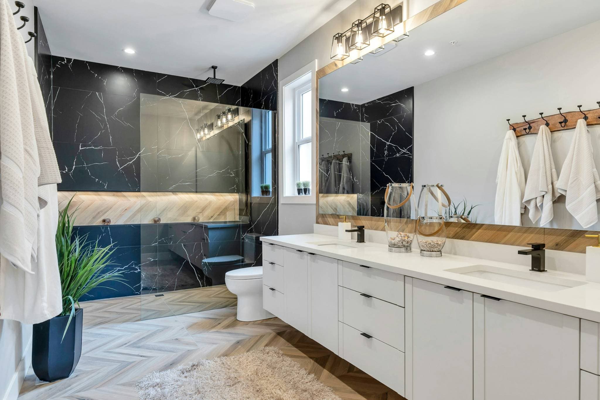 Emerald Ridge – Ensuite bathroom featuring a double vanity with white cabinets, large vanity mirror, dark marble tile shower wall, and chevron tile floor.