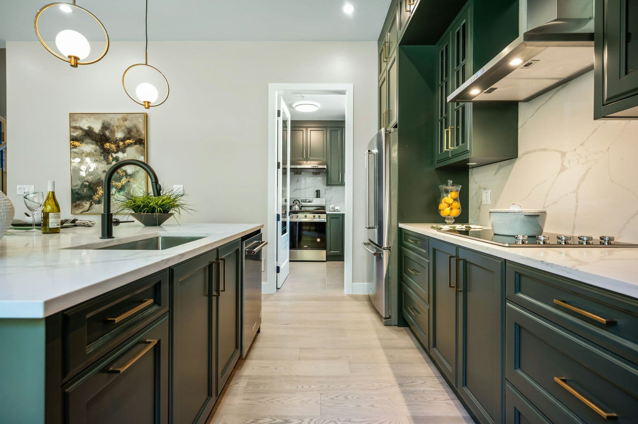 Emerald Ridge – Modern gourmet kitchen featuring dark green cabinetry, quartz countertops, gold hardware, stainless steel appliances, and a secondary spice kitchen pantry in view.