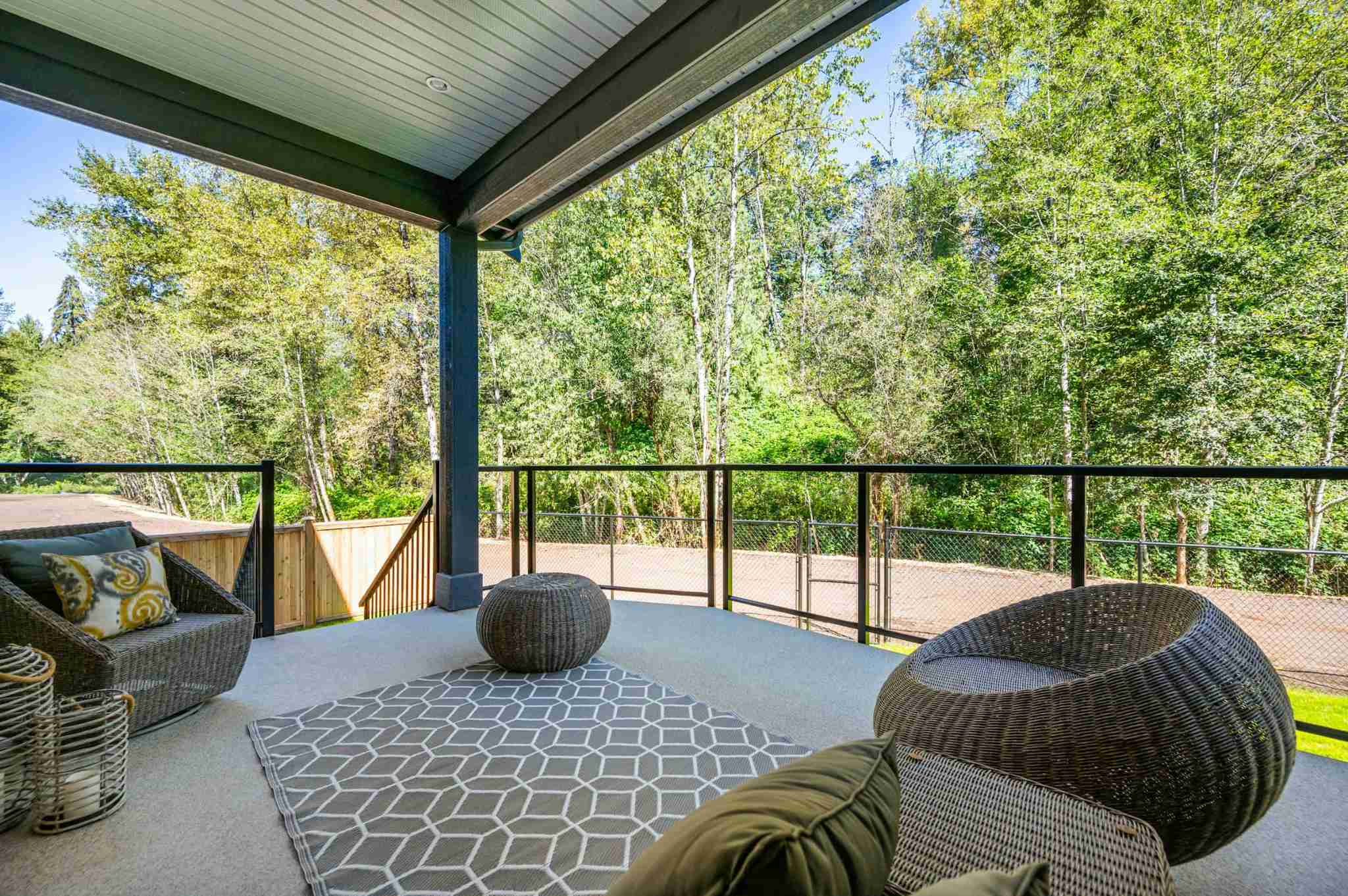 Emerald Ridge – View from a covered outdoor deck featuring wicker seating, outdoor rug, and glass railing looking into surrounding green trees.