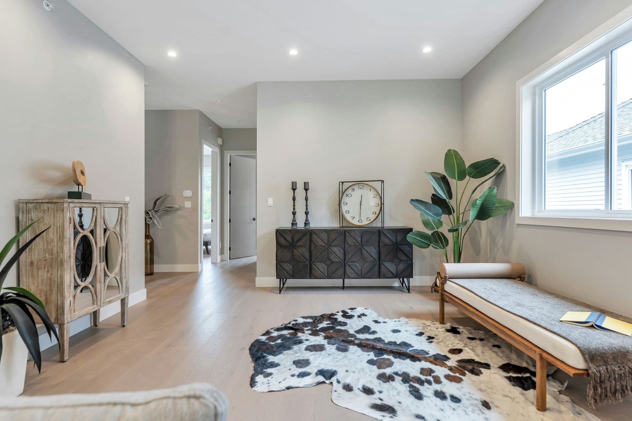 Emerald Ridge – Foyer or hallway seating nook with a dark carved sideboard, cowhide rug, daybed, potted plant, and light hardwood flooring.