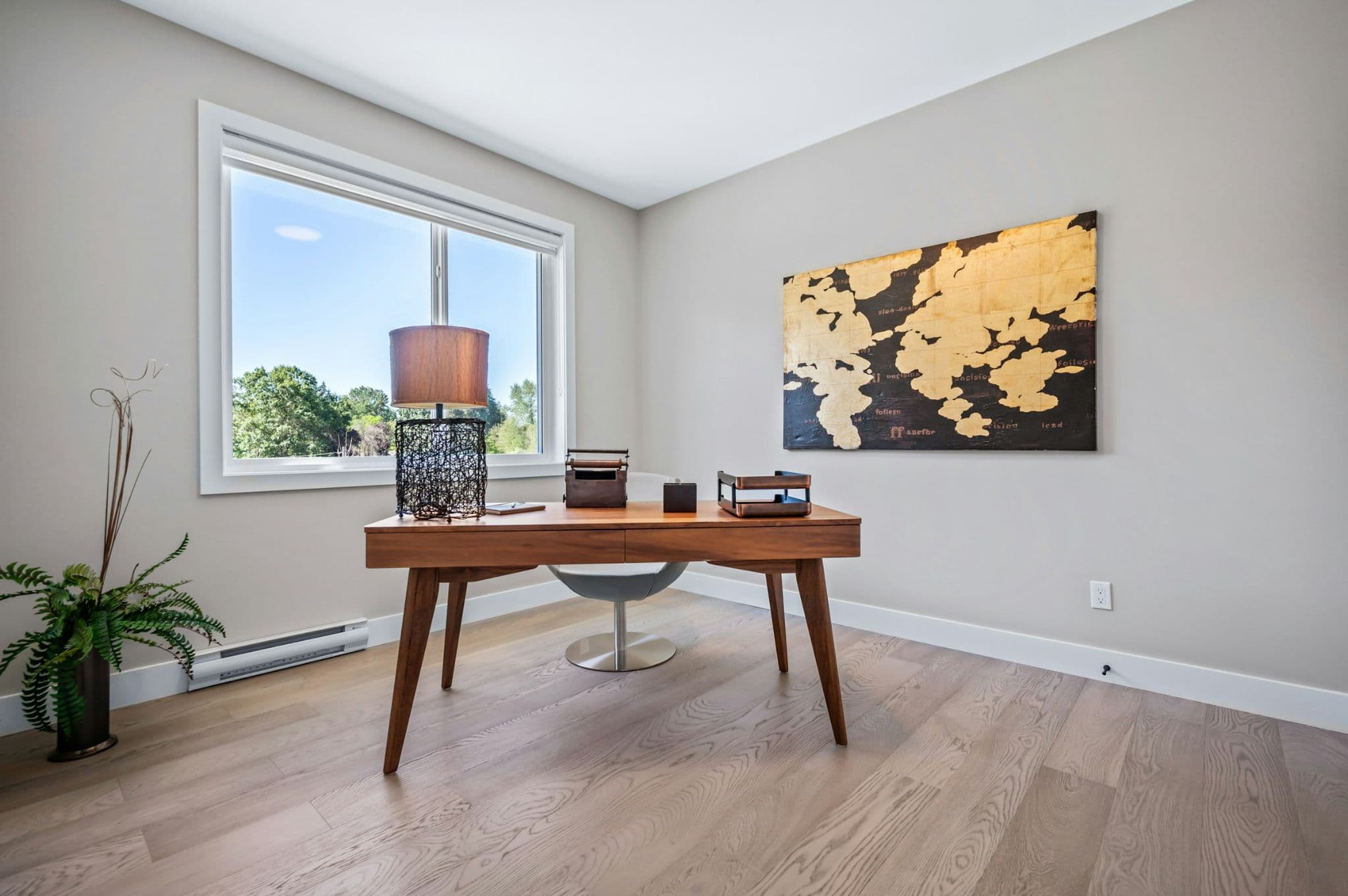 Emerald Ridge – Modern home office/den with mid-century wooden writing desk, gold world map canvas art, large window, and light wood flooring.