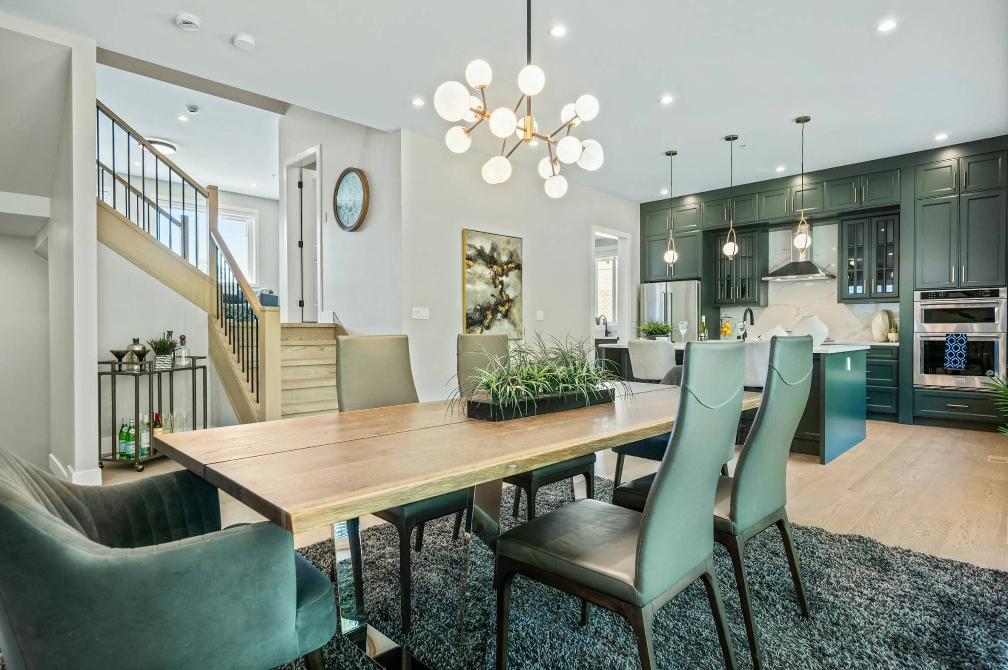 Emerald Ridge – Open-concept dining space with live-edge wood table, velvet armchairs, modern sputnik chandelier, and adjacent green kitchen.