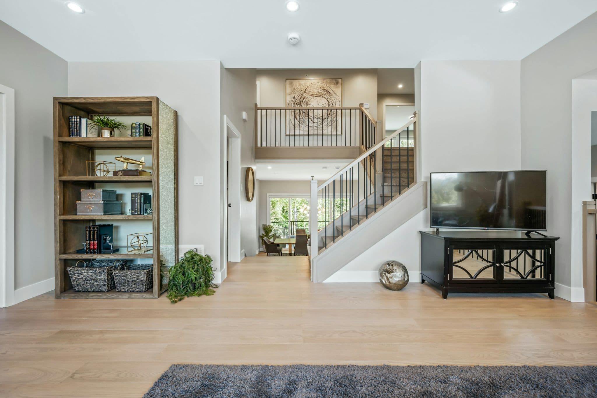 Emerald Ridge – Open hallway space showing a wooden bookcase, stairs leading to the upper landing, media console with TV, and entry corridor.