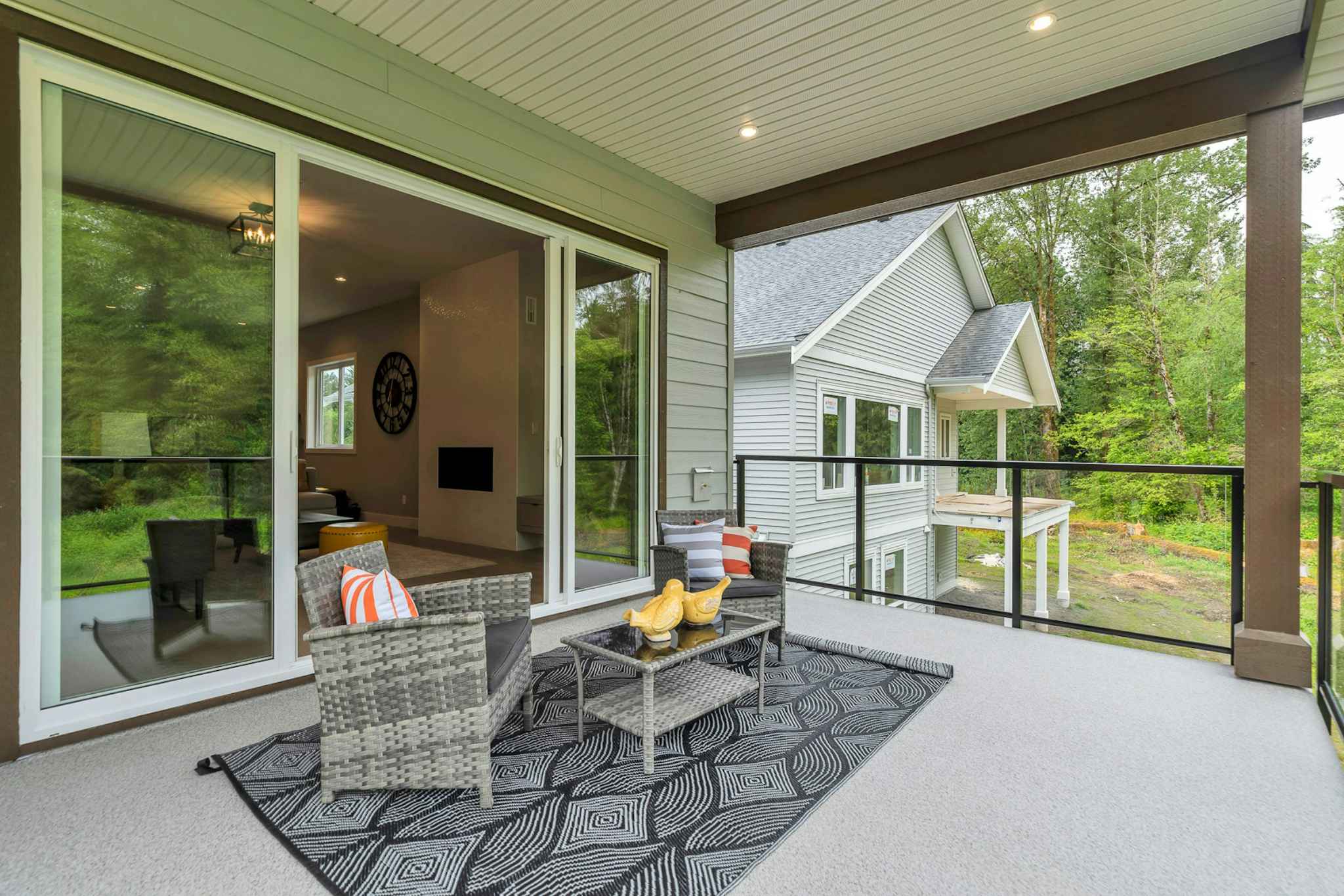 Emerald Ridge – Covered outdoor patio/balcony with patio armchairs, geometric rug, and glass railing opening up to sliding doors.
