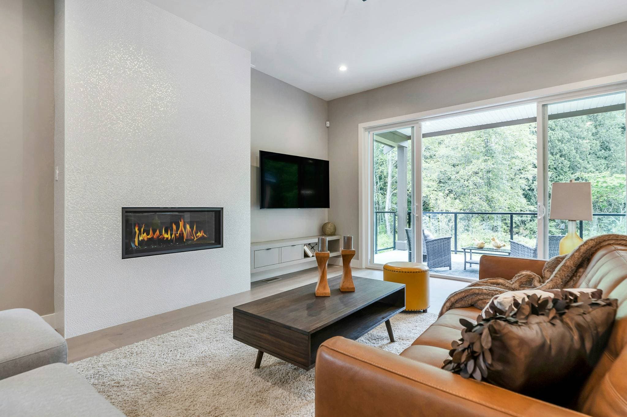Emerald Ridge – Cozy living room setting with a leather couch, dark wood coffee table, gas fireplace set into a textured white feature wall, and sliding doors to the deck.