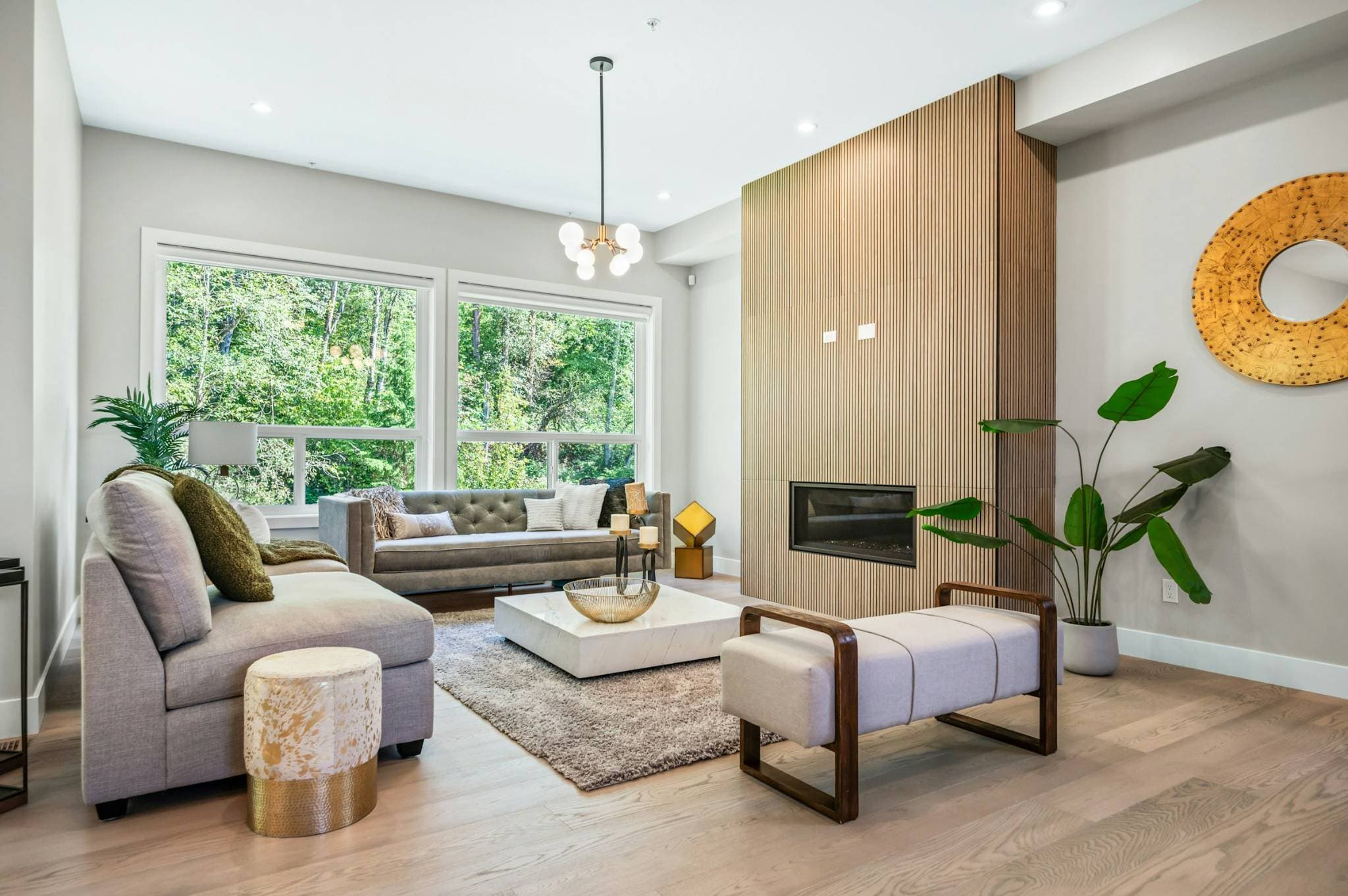 Emerald Ridge – Modern living room area featuring wood slat fireplace wall, grey sofas, marble coffee table, bench seat, and large windows.