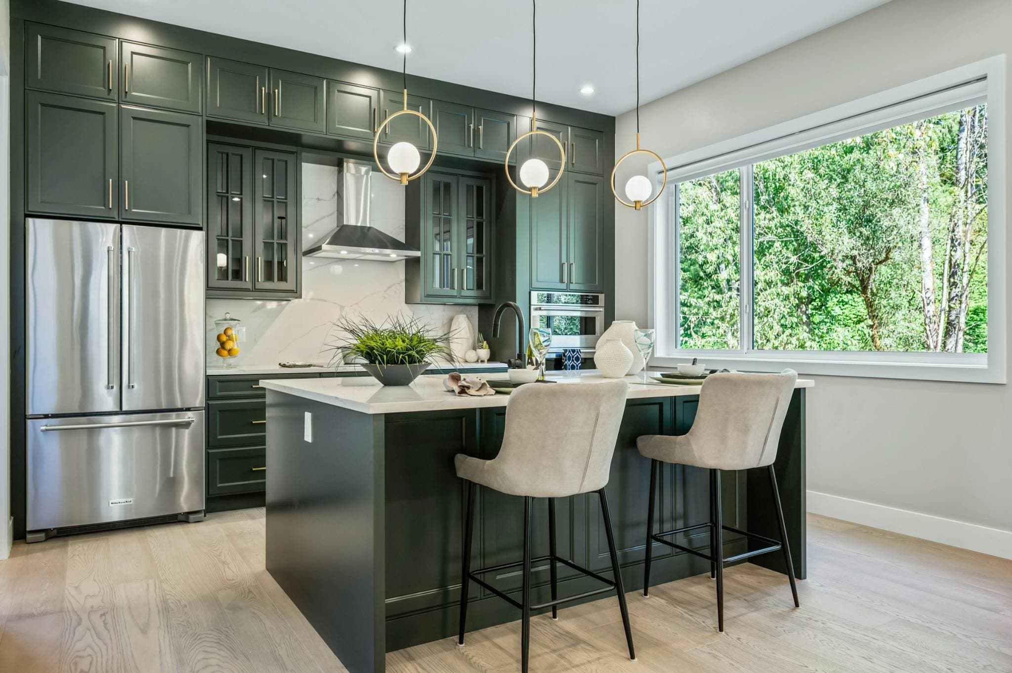 Emerald Ridge – Modern kitchen with dark green cabinetry, white quartz kitchen island, bar stools, ring pendant lights, and stainless steel refrigerator.