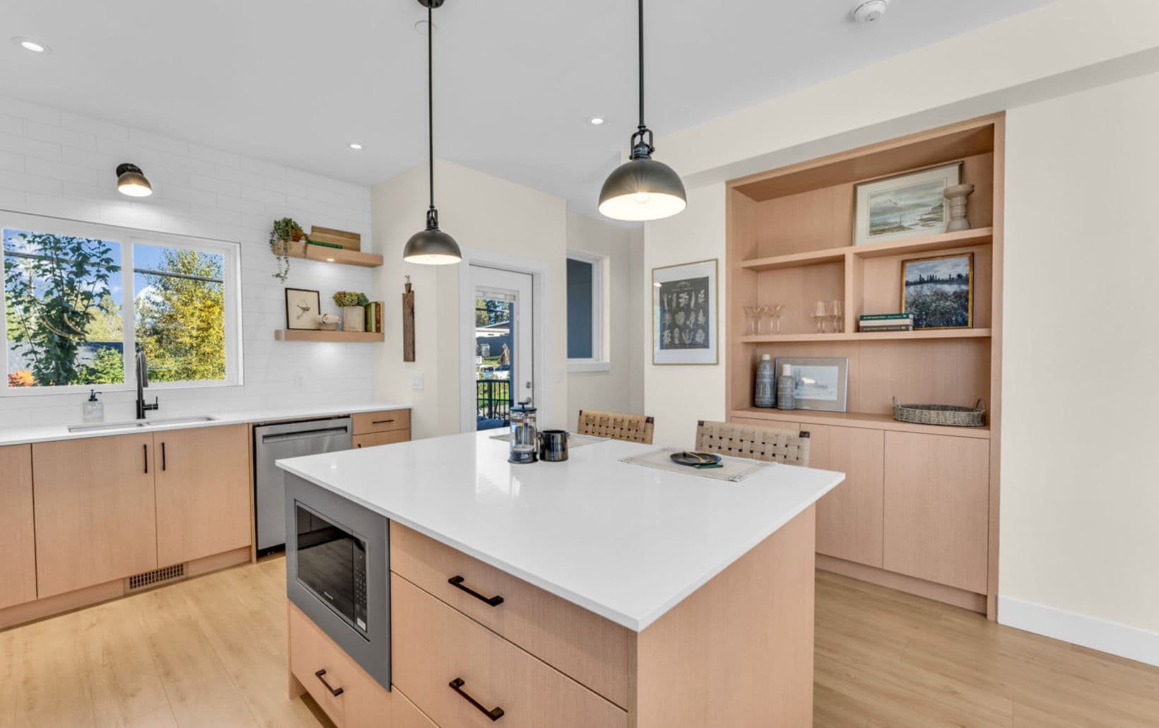 The Warwick – Kitchen with light wood cabinetry, an island with built-in microwave, white subway tile backsplash, pendant lights, and open wood shelving with decor beside the island.