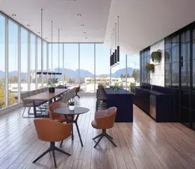 Georgetown One – A modern, sunlit penthouse lounge featuring light wood flooring, a long wooden dining table, small seating arrangements with leather armchairs, and a dark island kitchen with sleek black pendant lighting. Floor-to-ceiling glass windows surround the space, offering panoramic views of surrounding green hills and mountains under a clear daytime sky.