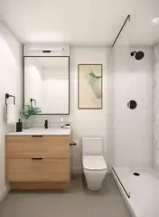 Georgetown One – A modern, bright bathroom featuring a light wood vanity with a white countertop, black hardware, a large rectangular mirror, and a sleek glass-enclosed walk-in shower. The space is finished with clean white walls, neutral floor tile, a simple framed art piece, and soft vanity lighting.