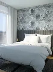Georgetown One – A modern bedroom featuring a neatly made bed with light gray linens, an upholstered dark gray headboard, and a striking black-and-white cloud patterned wallpaper backdrop. Floor-to-ceiling windows with sheer white drapes fill the bright space with natural daylight.