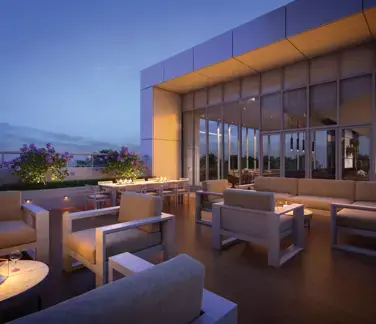 Georgetown One – A luxurious outdoor rooftop terrace lounge is captured at twilight, featuring comfortable modern sofas, armchairs, and a dining table with integrated fire pits. Warm recessed lighting illuminates the deck, planter boxes with purple flowers, and a covered glass-walled indoor pavilion under a deep blue evening sky.