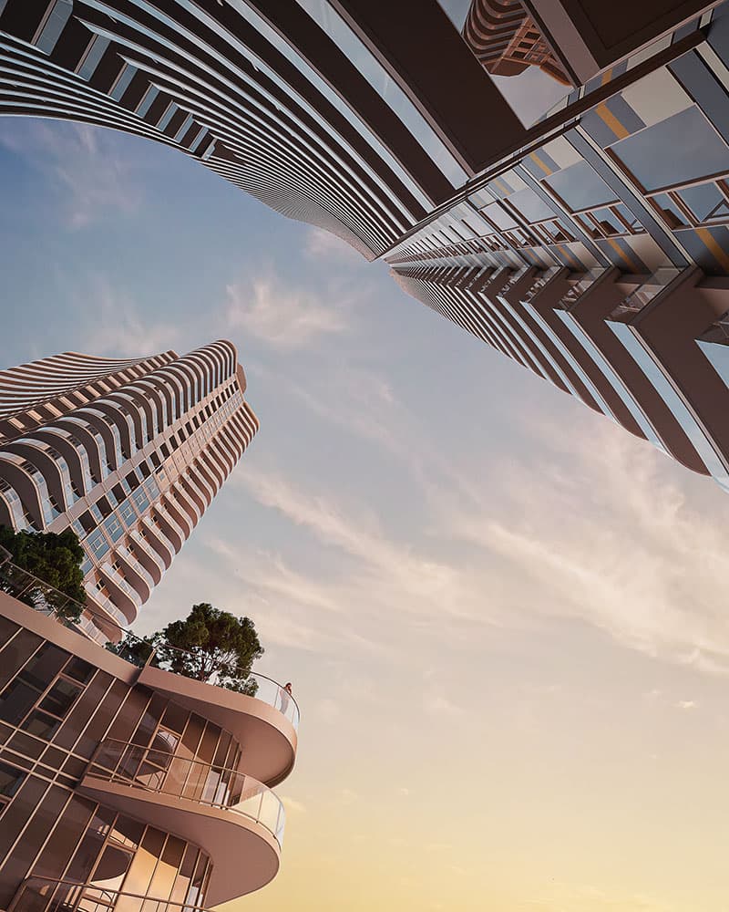 Piano – A dramatic worm's-eye view looking up between modern residential high-rises featuring curved balconies and glass facades. An elevated terrace podium holds lush green trees against a pale sunset sky with wispy clouds.
