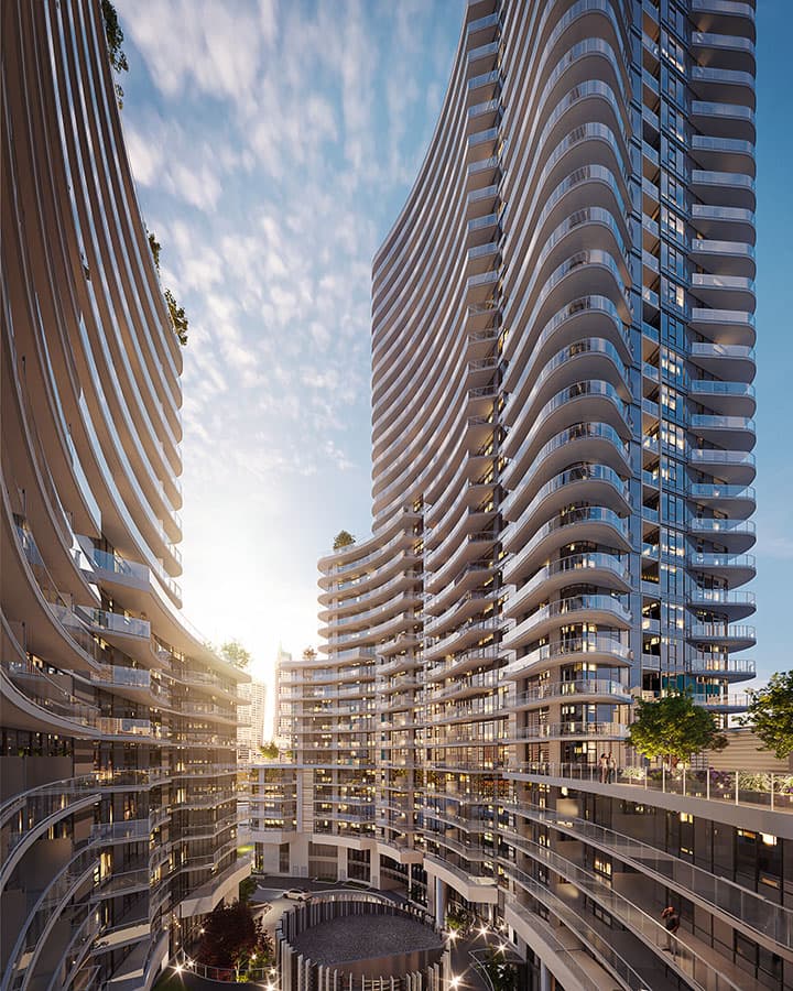 Piano – A high-angle exterior perspective of a modern residential complex featuring towering high-rises with dramatic, undulating white balconies and glass railings. The towers flank a central landscaped courtyard and driveway below, illuminated by warm sunlight bursting between the structures under a partly cloudy sky.