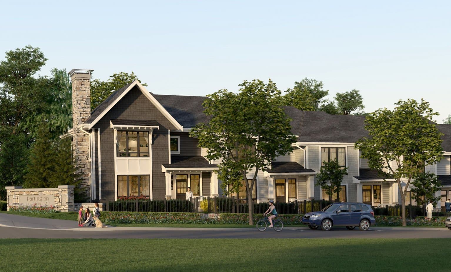 Partington Creek – Street-level view of a two-storey craftsman-style townhome with a stone chimney, showing the Partington Creek entrance sign, a cyclist, and pedestrians with a dog.
