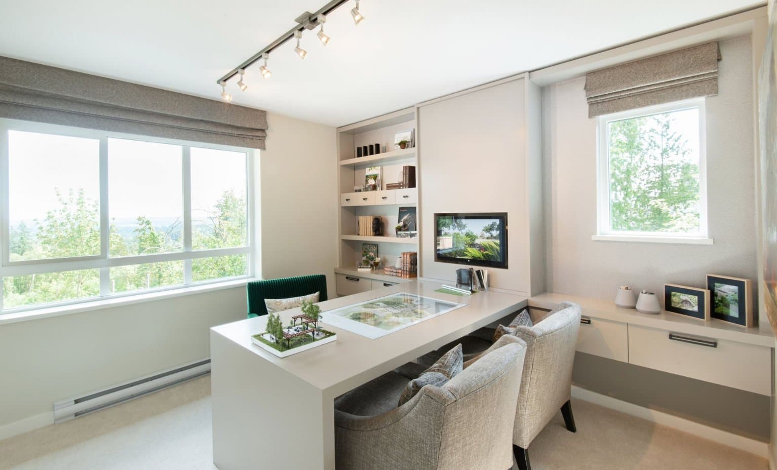 Partington Creek – Sales-office style room with a built-in shelving unit, wall-mounted screen, and a desk displaying an architectural site model and plans.