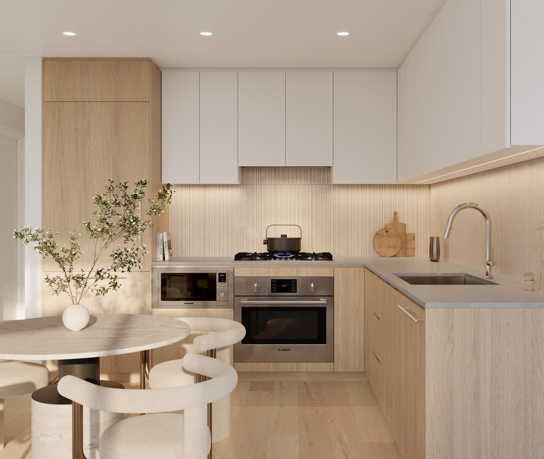 Ethos – A modern residential kitchen featuring light wood lower cabinets, white upper cabinetry, and a textured ribbed backsplash with warm under-cabinet lighting. Adjacent to the stainless steel appliances is a round marble dining table paired with curved, light-upholstered chairs.