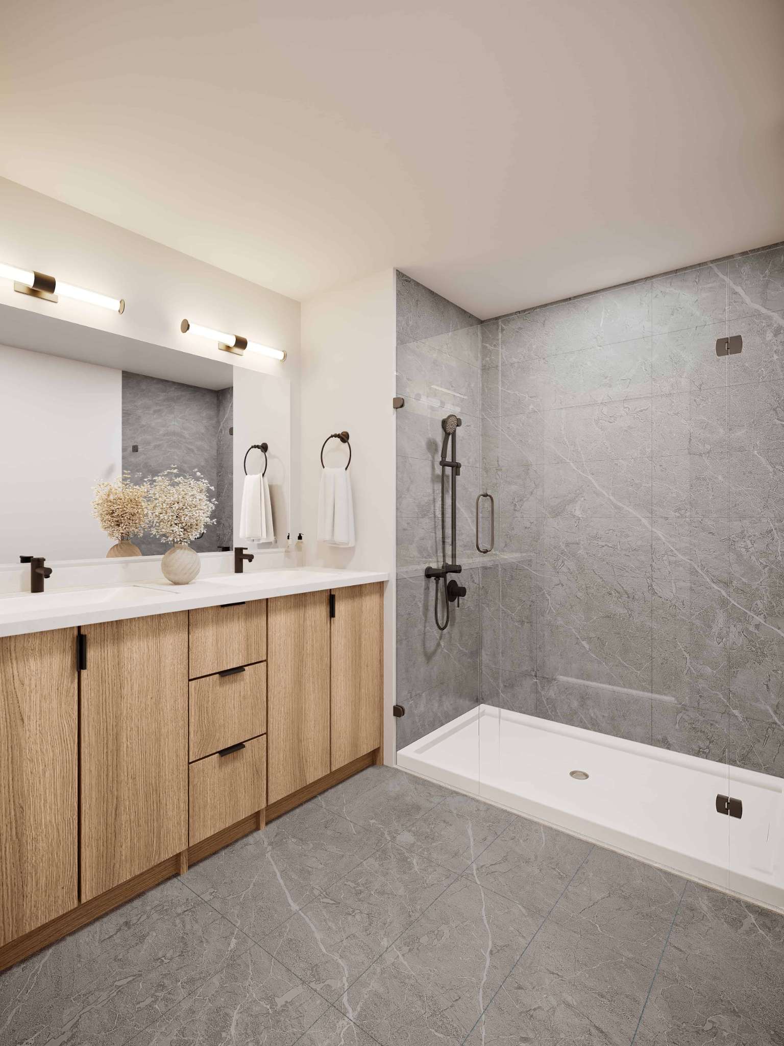 Eden Townhomes – A bathroom with a double sink vanity in light wood, a large mirror, and a walk-in glass shower with grey stone tile.