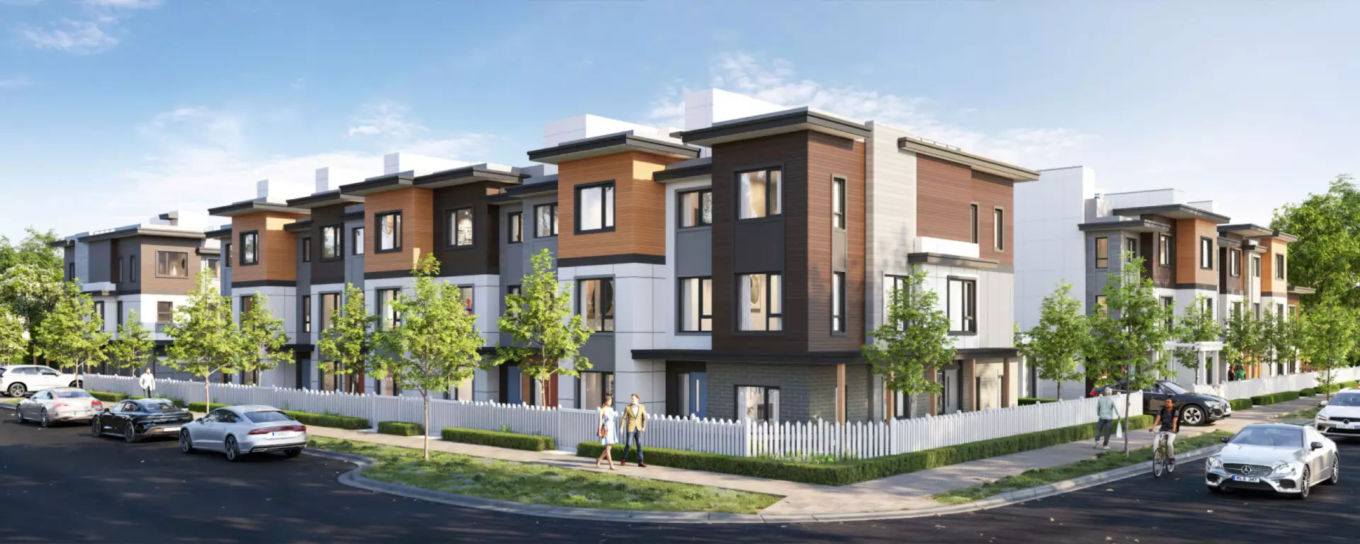 Eden Townhomes – Street-level view of a row of modern three-story townhomes with wood and grey siding, behind a white picket fence, with pedestrians and cars on the street.