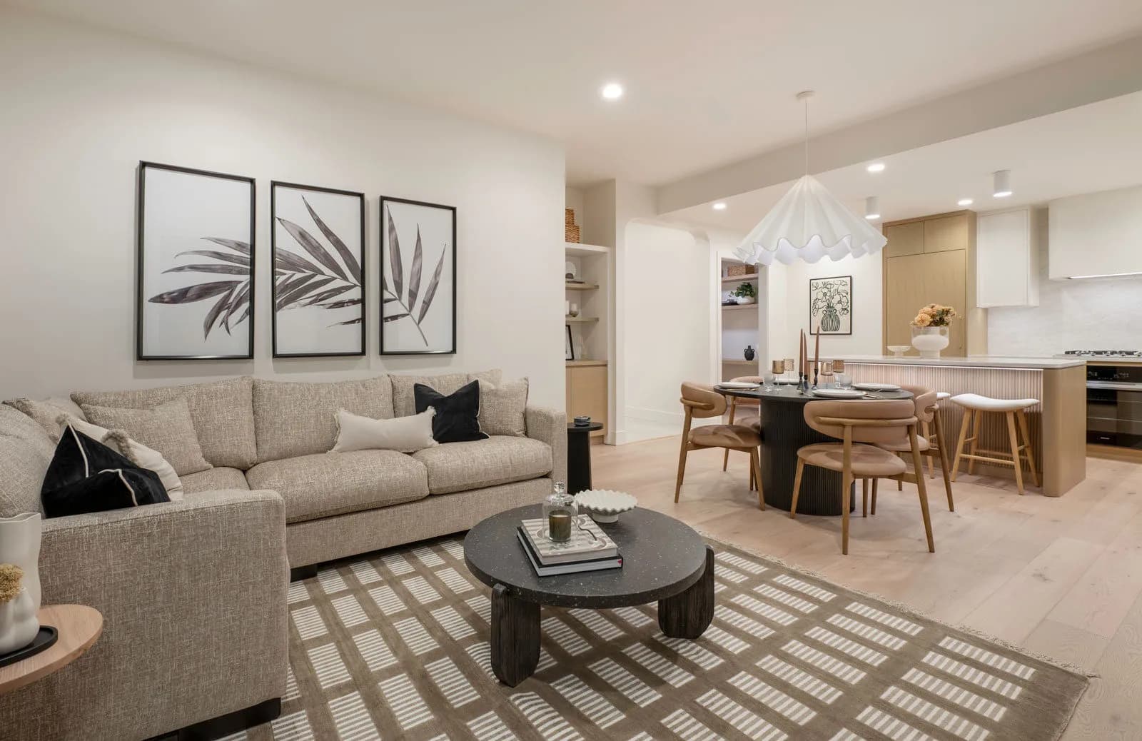 Rhodes – Staged open-plan living and dining room flowing into a light-wood kitchen, with wide-plank hardwood floors and a sectional sofa.