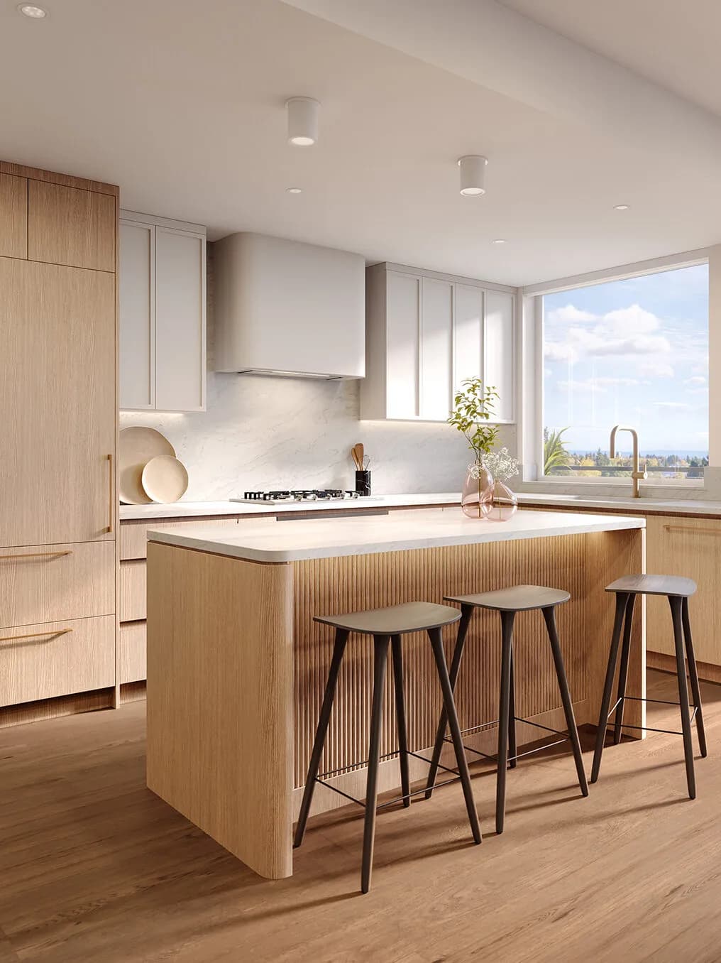 Rhodes – Kitchen with fluted light-oak island, three bar stools, white stone counters and a large window with an outlook over trees toward the water.