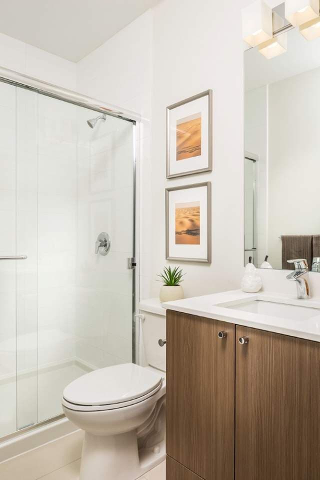 Allwood Place – Bathroom with a glass-enclosed shower/tub, a wood vanity with a white countertop, framed desert-toned art, and a toilet.